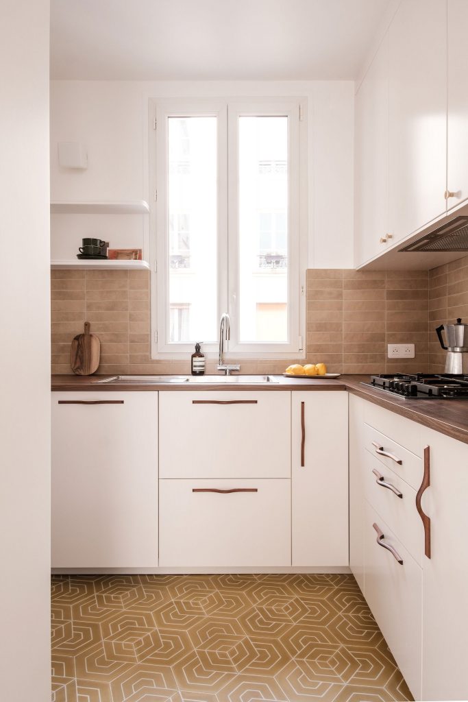 Cuisine avec façades blanches, poignées en bois sculpté et sol en carreaux géométriques jaunes