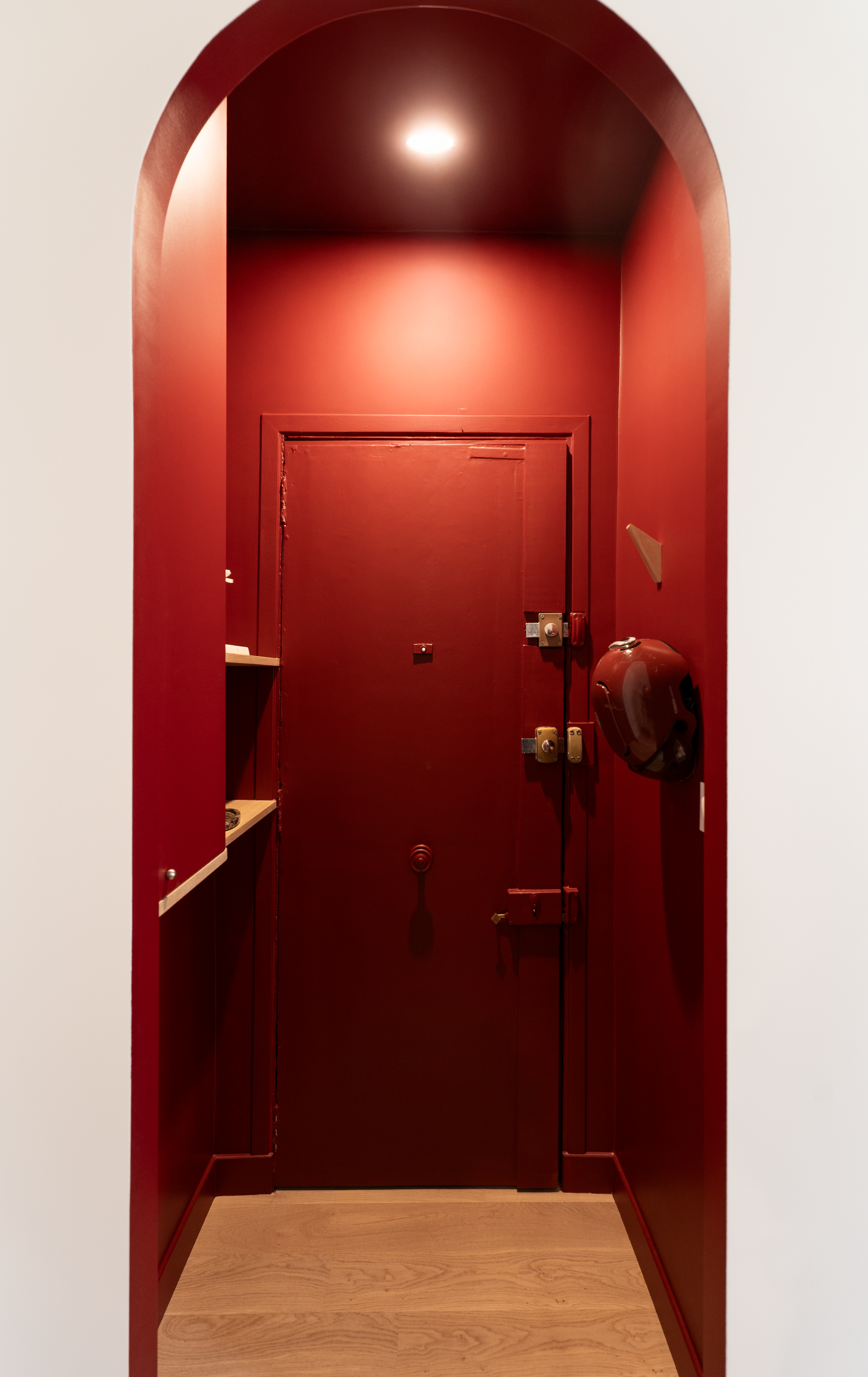 Entrée d’appartement rénovée avec arche peinte en rouge et porte ancienne conservée
