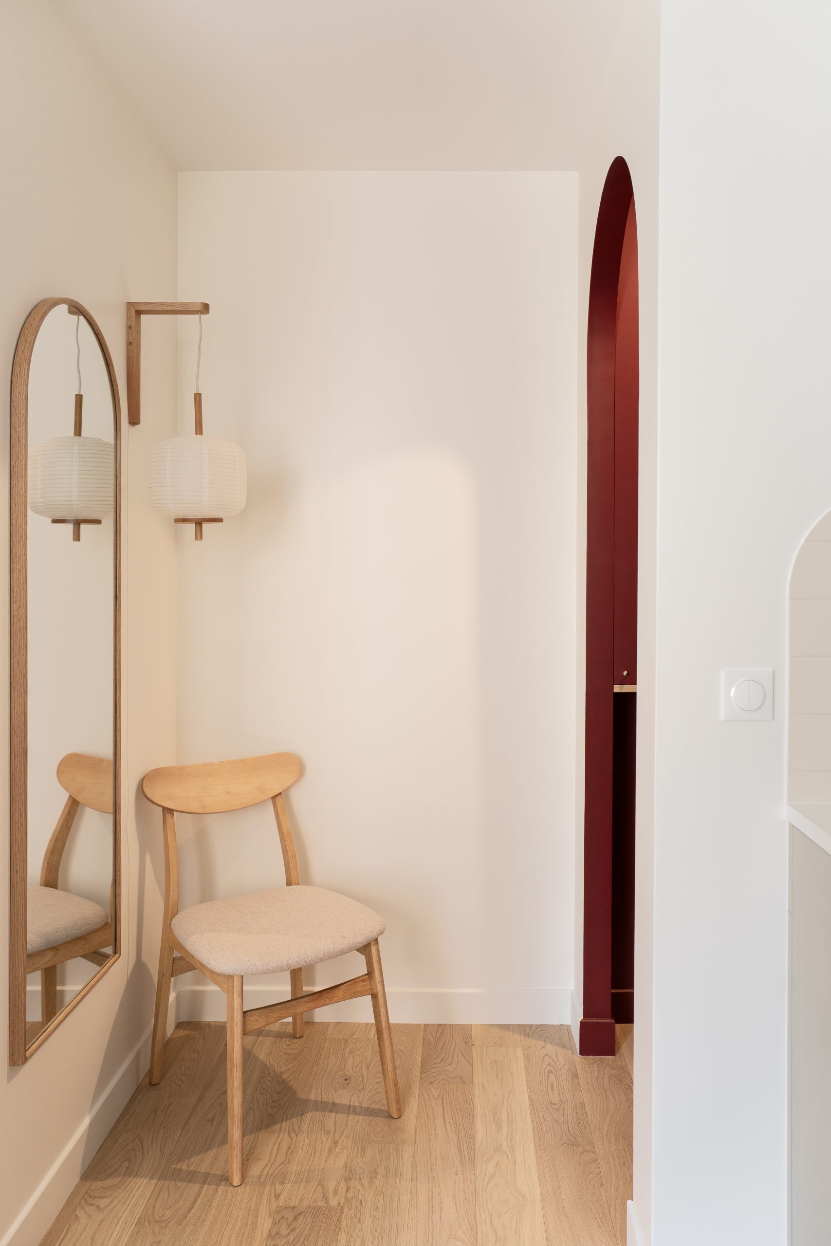 Coin entrée avec chaise en bois, miroir mural et arche rouge décorative