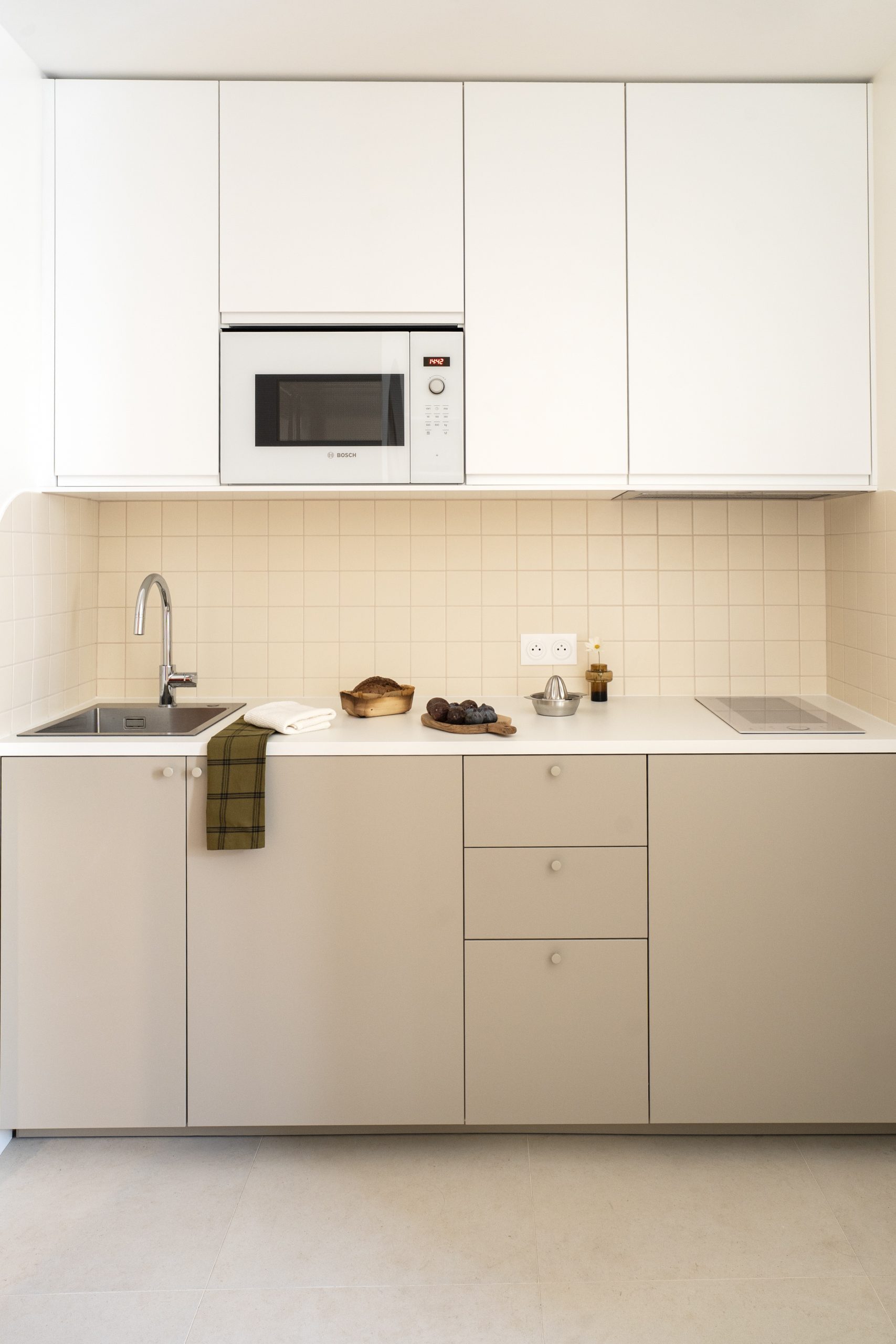 Cuisine moderne rénovée avec meubles beige, crédence en petits carreaux et électroménager encastré