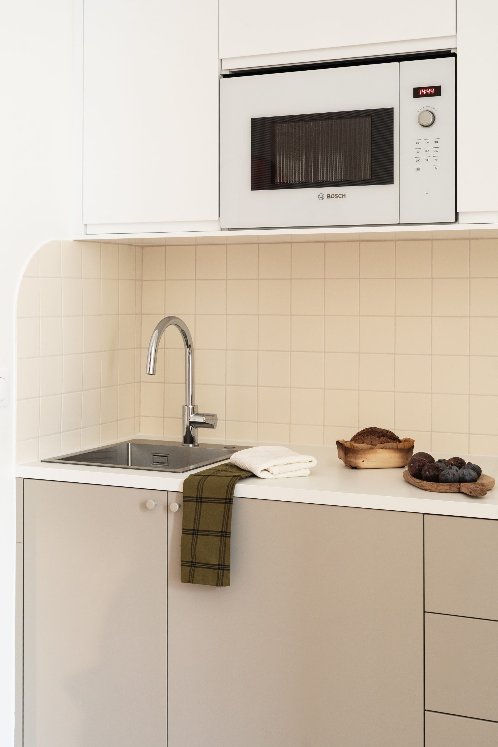 Détail de cuisine rénovée avec évier inox, plan de travail clair et crédence carrelée