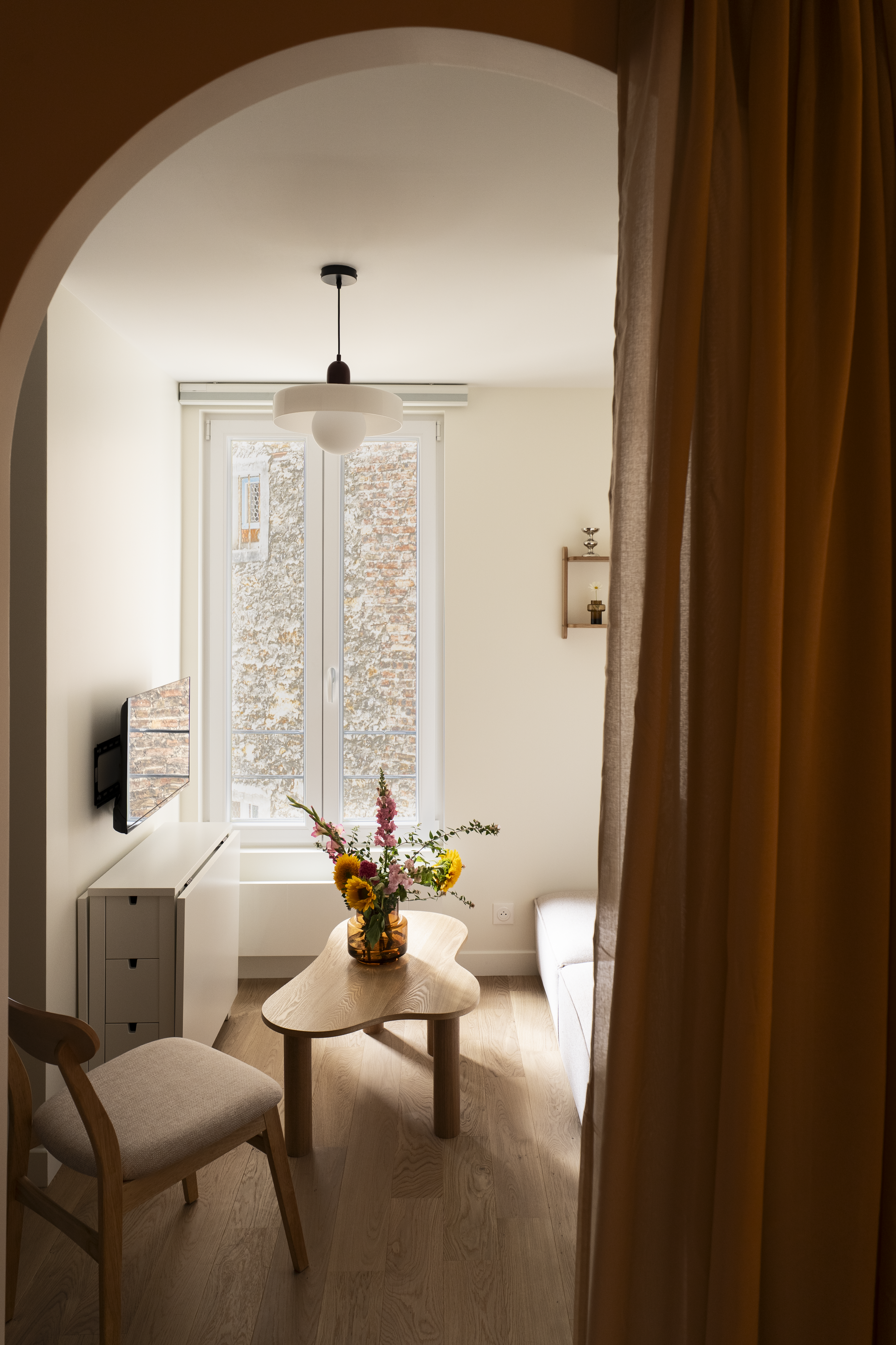 Vue du séjour depuis le coin nuit avec arche, table basse en bois et lumière naturelle dans un studio rénové