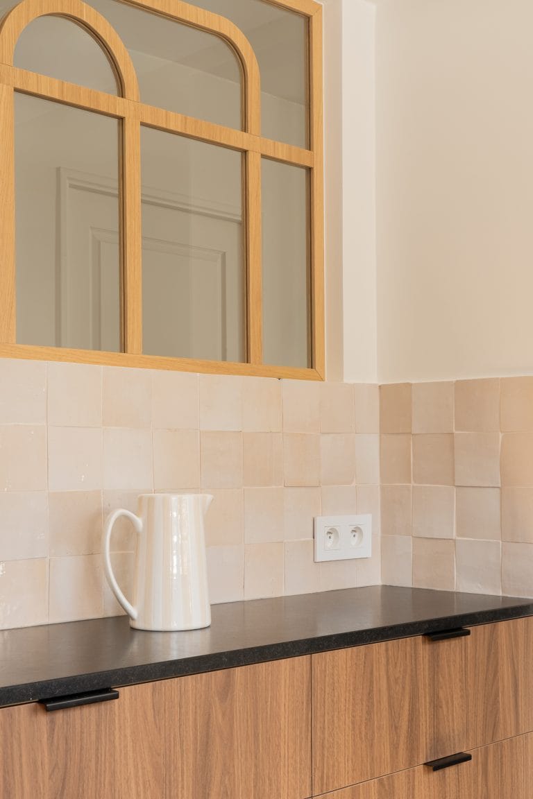 Détail d'une verrière en bois cintrée au-dessus d'une crédence en zellige beige, avec pichet en céramique