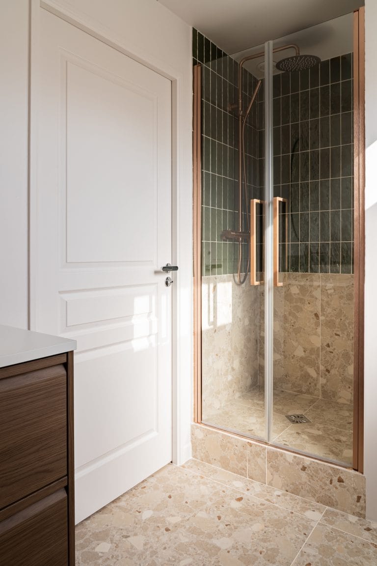Douche à l'italienne avec carrelage vert en faïence, sol et murs en terrazzo beige et robinetterie cuivrée