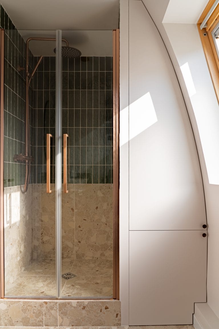 Cabine de douche vitrée à cadre cuivré installée sous une pente de toit, avec fenêtre de toit