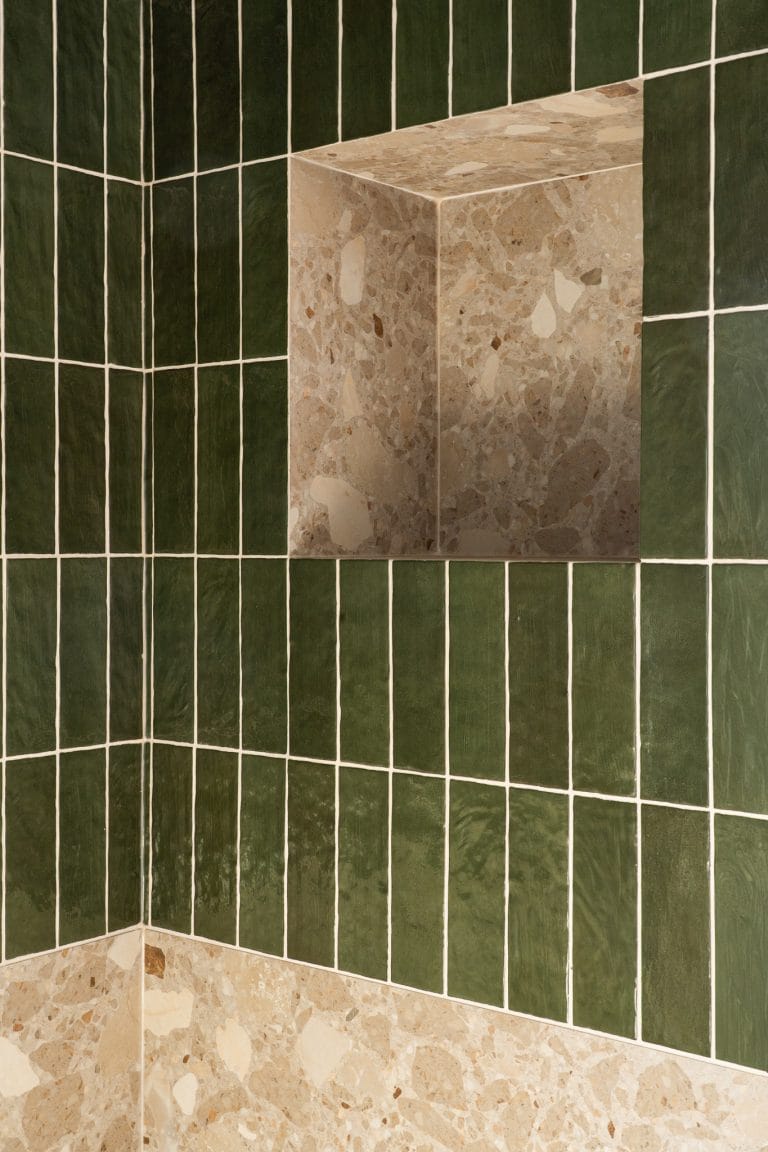 Détail d'une niche de douche en terrazzo beige encastrée dans un carrelage vert en faïence