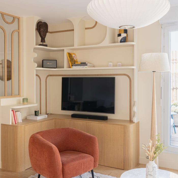 Salon avec bibliothèque murale sur mesure aux formes arrondies, TV intégrée, fauteuil terracotta et tapis berbère