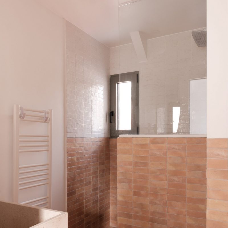 Salle de bain avec faïence blanche et carrelage en terre cuite, ambiance méditerranéenne.