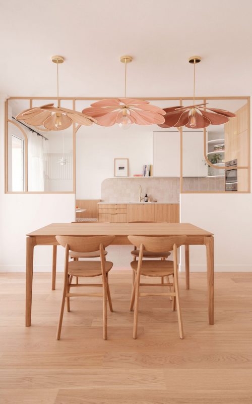 Vue sur une salle à manger élégante avec suspension en pétales et grande verrière donnant sur la cuisine.