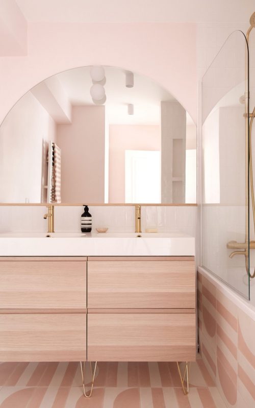 Salle de bain avec meuble en bois, double vasque et miroir arrondi, dans des tons pastel doux.