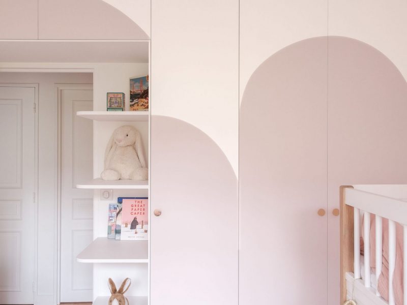Chambre d’enfant avec dressing blanc aux portes arrondies et décor mural coloré.