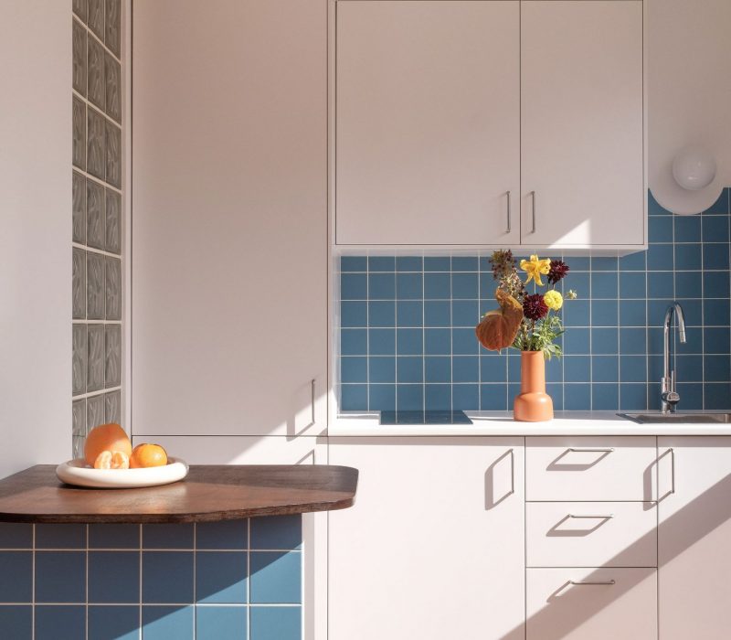 Cuisine rénovée avec carrelage bleu et meubles blancs dans un studio lumineux