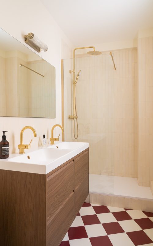 Salle de bains avec double vasque bois, robinetterie laiton et sol damier rouge et blanc